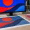 Monitor showing saturated artwork next to the duller printed version and a Pantone fan